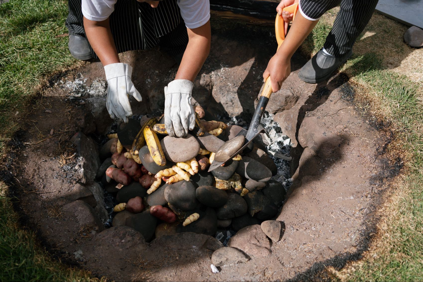 Women at the Parwa Community Restaurant in Lamay, Peru, preparing an earth oven for pachamanca