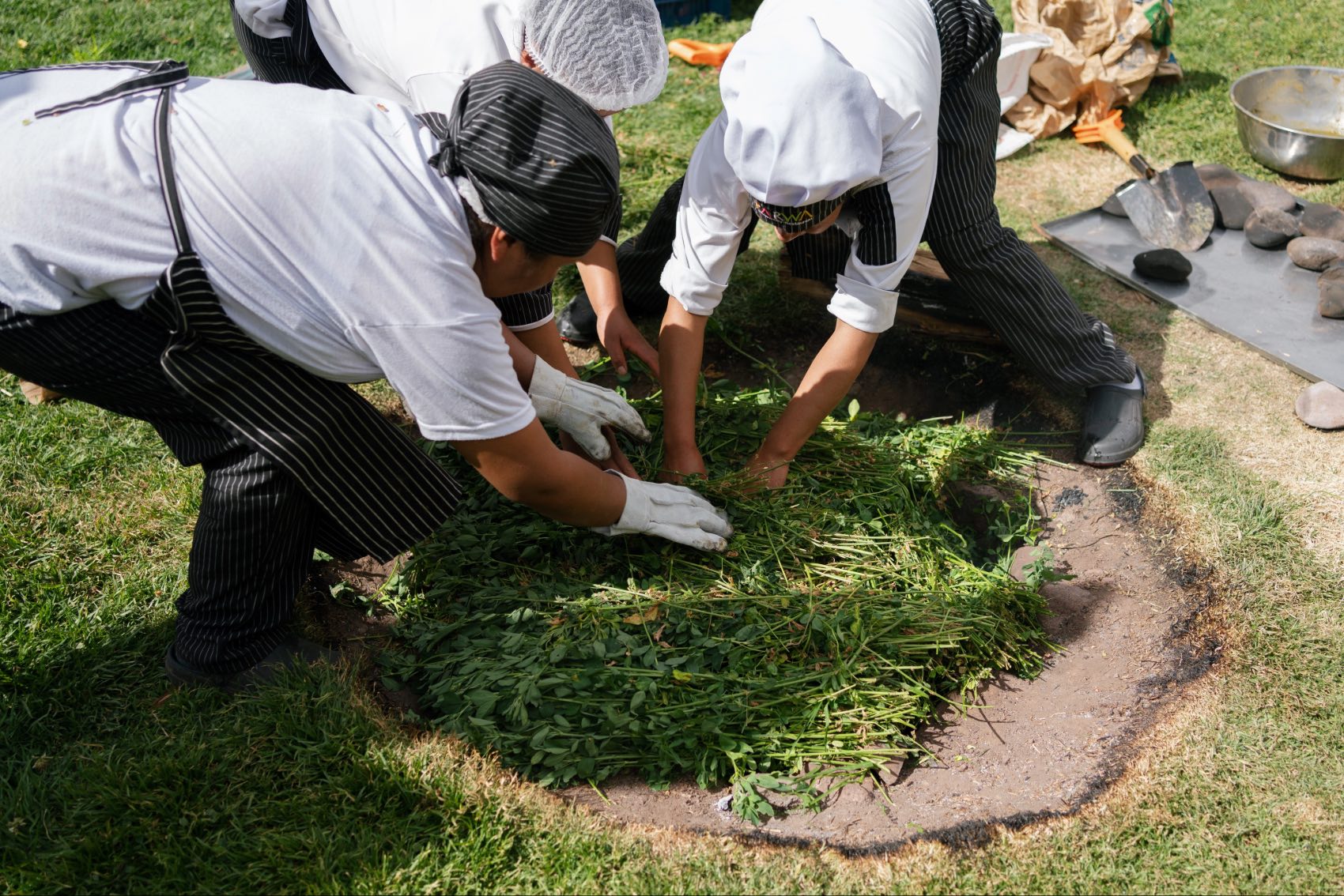 Women at the Parwa Community Restaurant in Lamay, Peru, preparing the earth oven for pachamanca