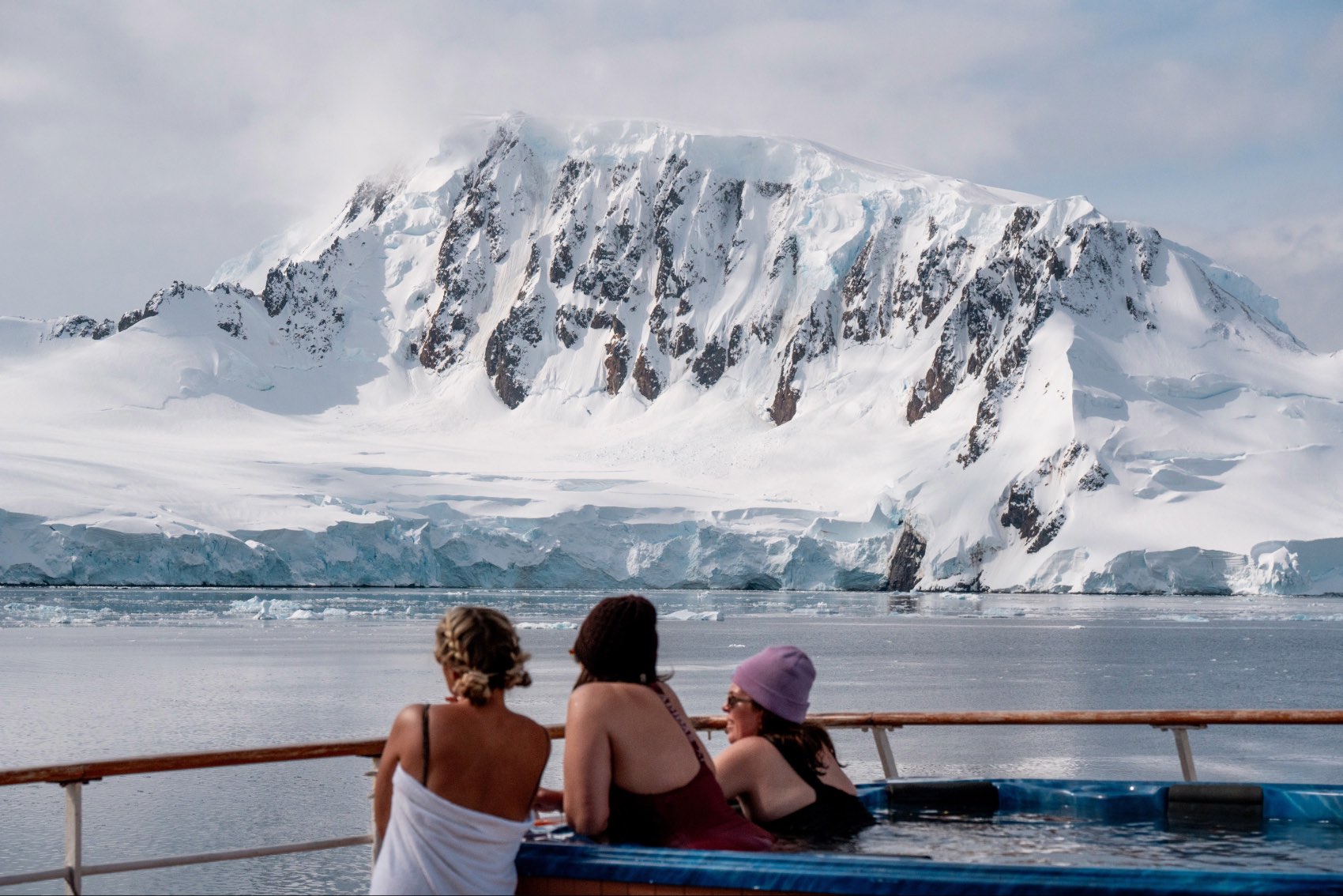 Three people gazing out at the view of an Antarctica iceberg