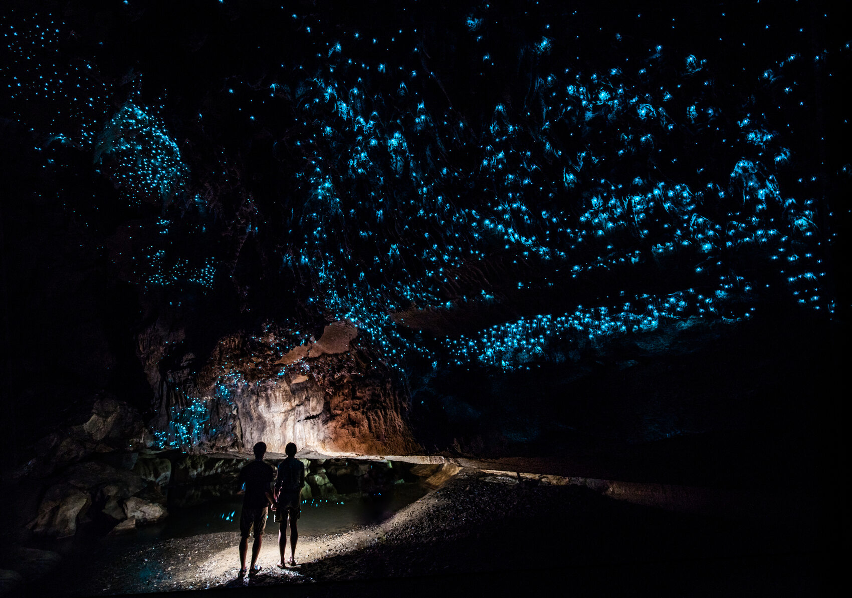 A couple standing underneath Glow Worm Sky in Waipu Cave in New Zealand