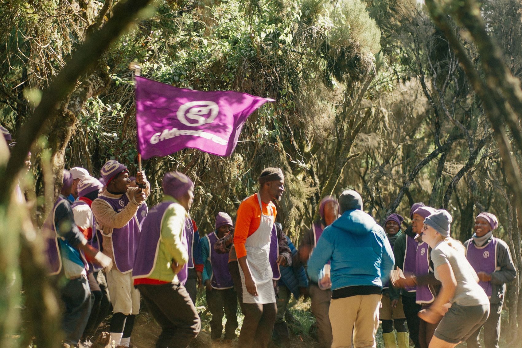 A group of people with a G Adventures flag after completing their Mt. Kilimanjaro tour