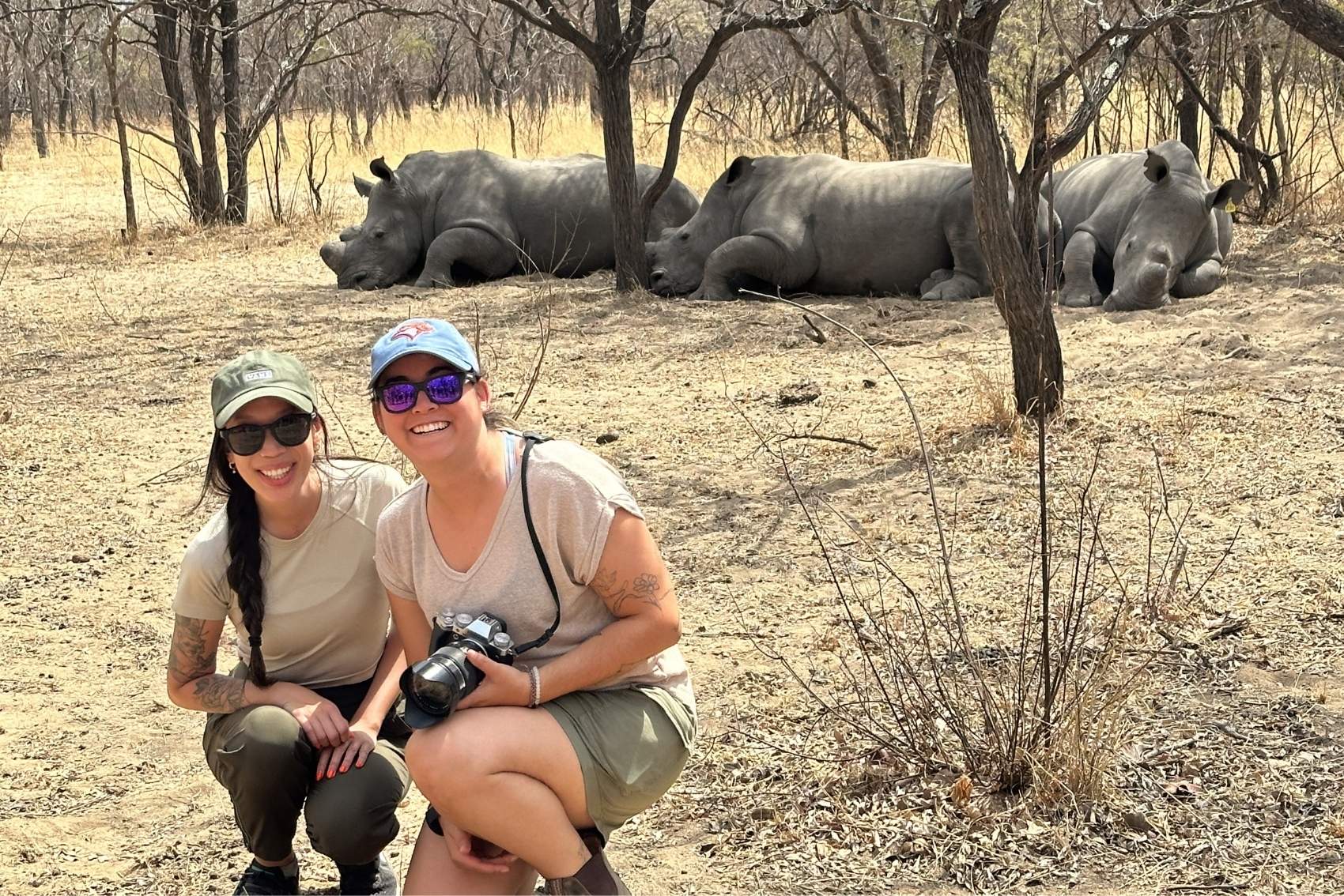 Ana and her friend crouching in front of rhinos in Southern Africa