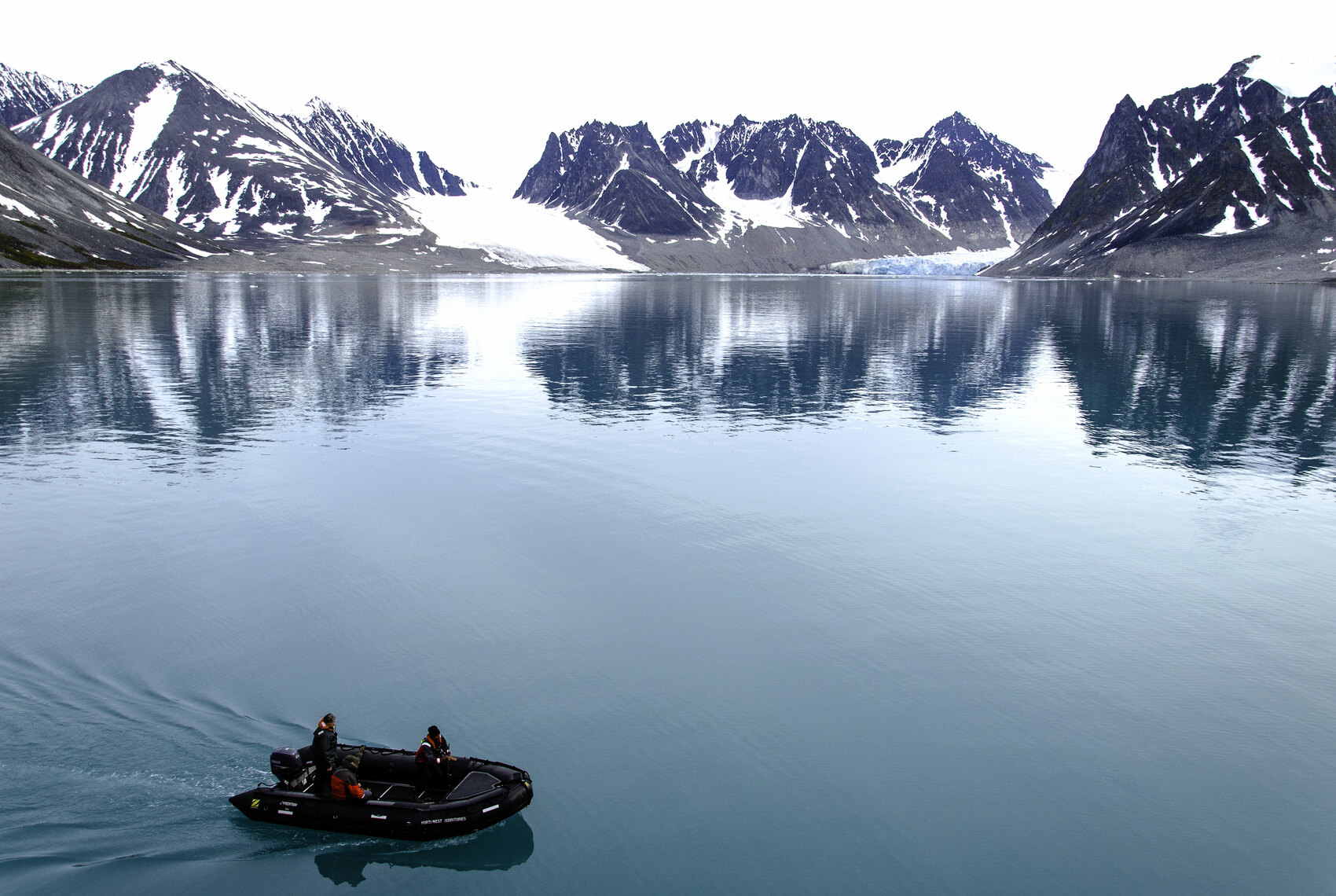 A dingy with staff driving it sailing through the waters of the Arctic near mountains